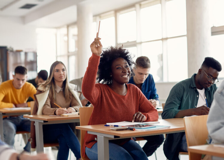 Happy African American student raising her hand to ask a question during lecture in the classroom.